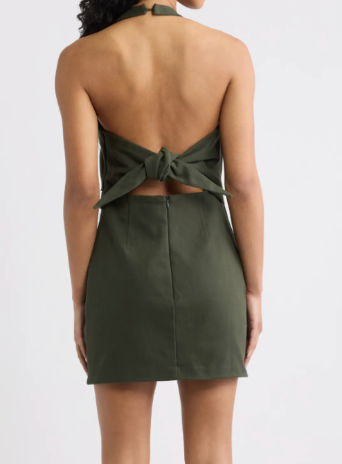 A woman shown from the back wearing an olive green halter mini dress with a tie-back detail and a high-waisted, straight skirt.