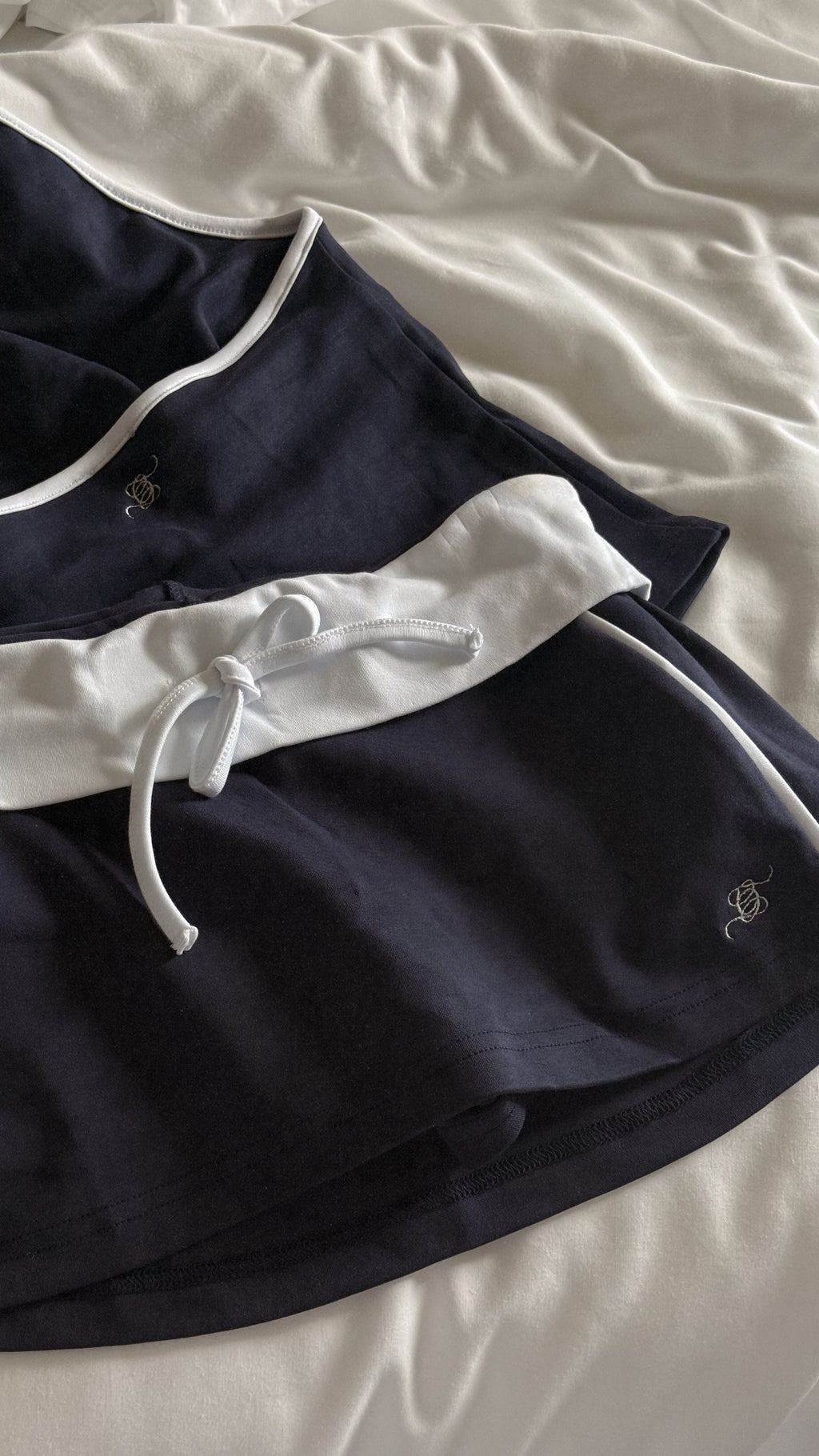 A pair of navy blue shorts with white trim and a white drawstring, laid flat on a white bedsheet background.