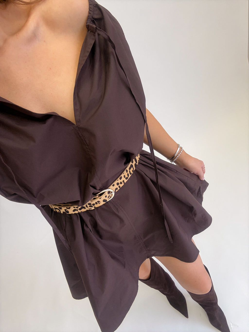 A person wearing an oversized dark brown wrap-style dress with a leopard-print belt and matching pointed-toe boots, photographed against a plain light background.